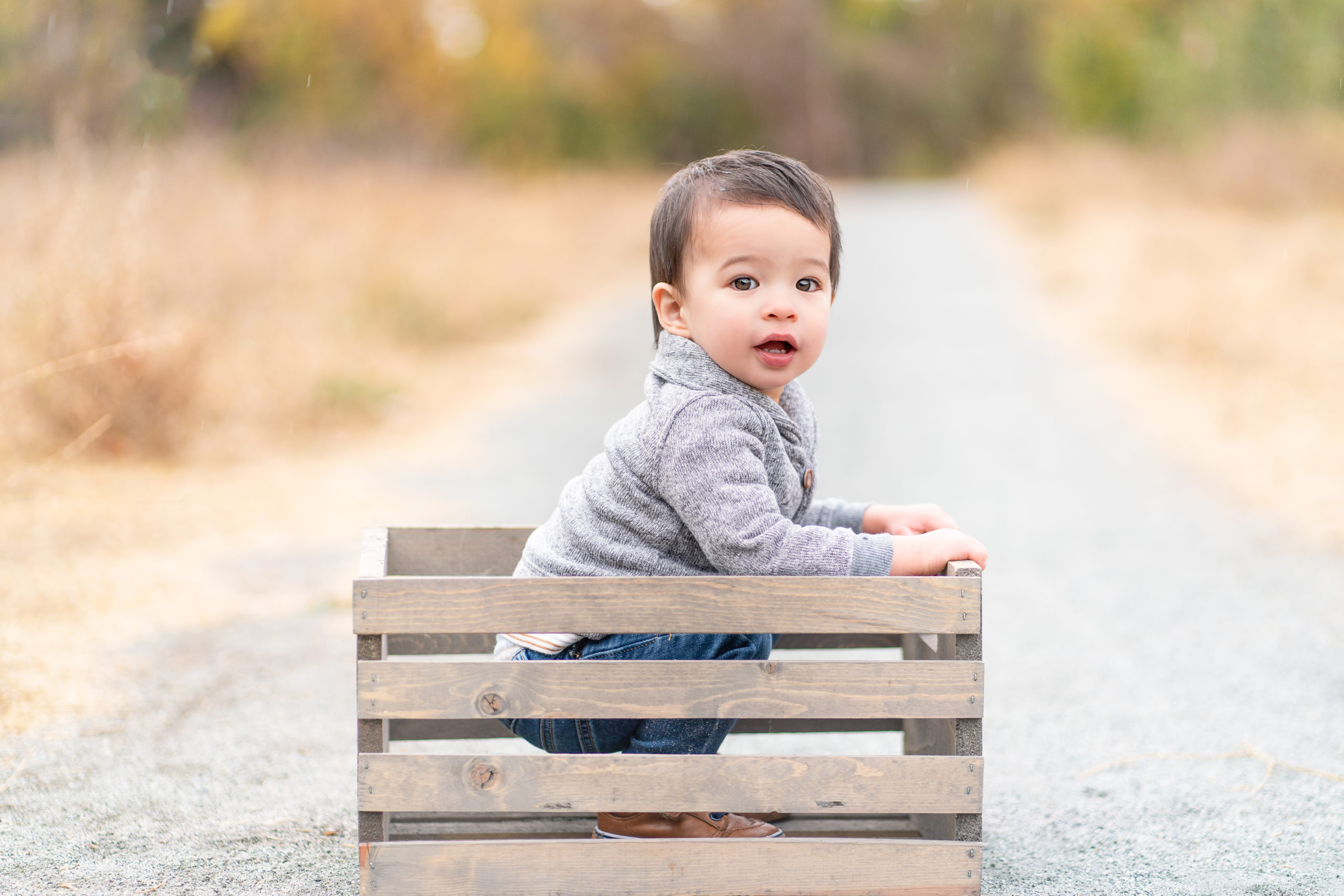 little boy outdoors sitting in a wooden crate