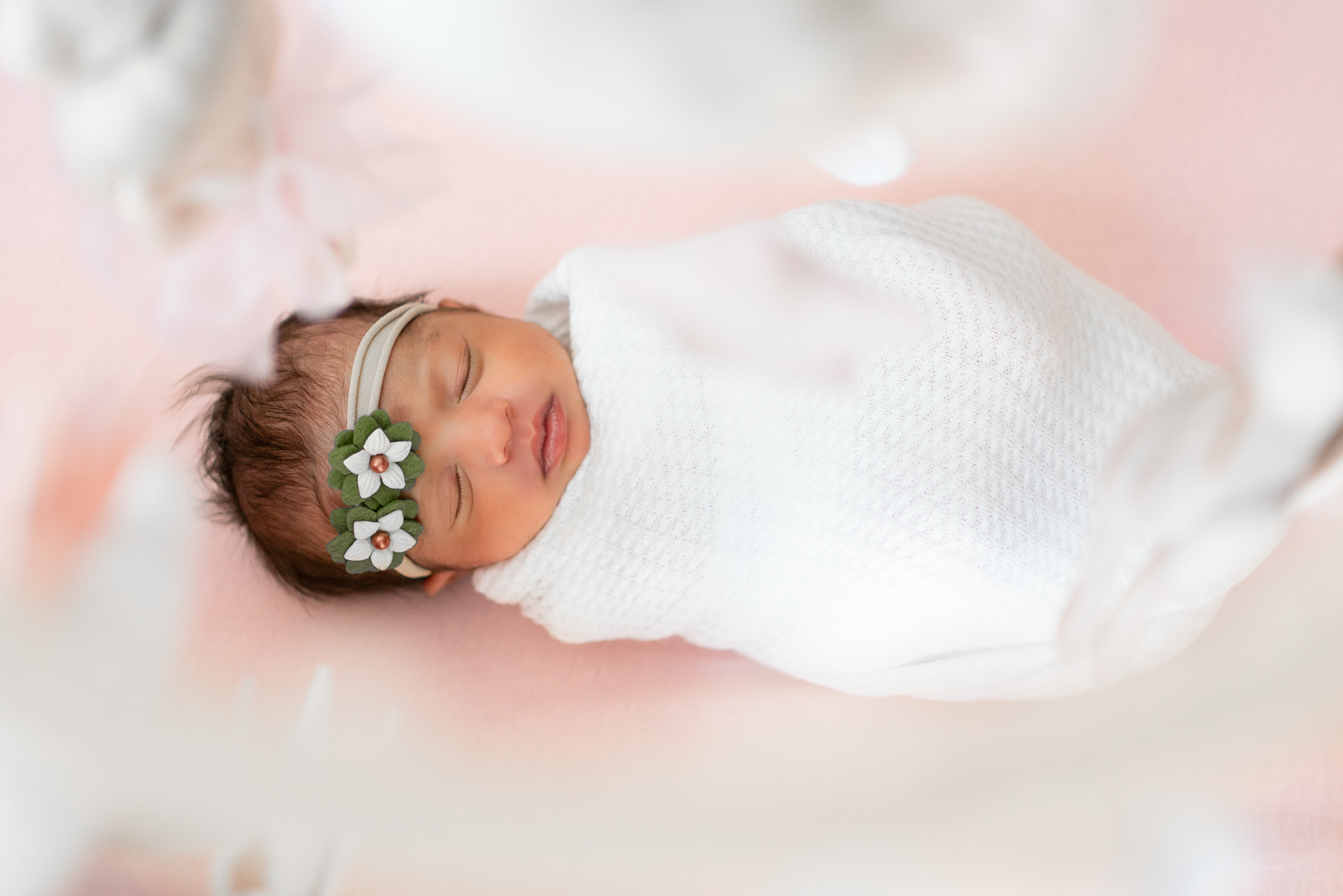 newborn girl swaddled in white lying on a pink crib sheet
