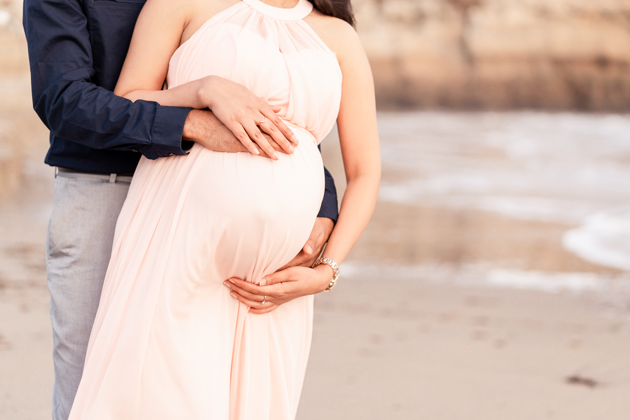 closeup of pregnant women's belly with husband's arms wrapped around her holding belly