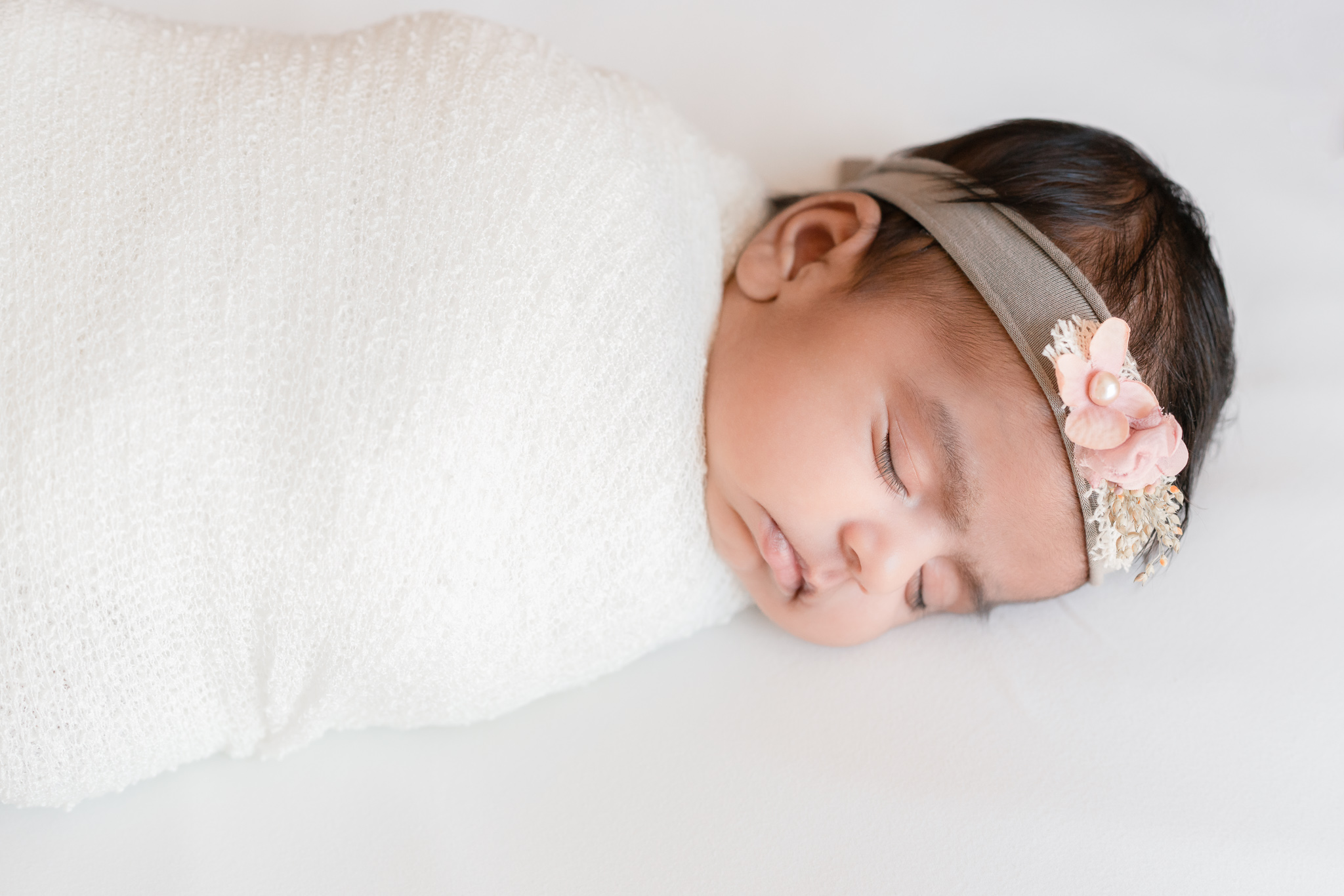 sleeping newborn baby girl swaddled in white with a floral headband