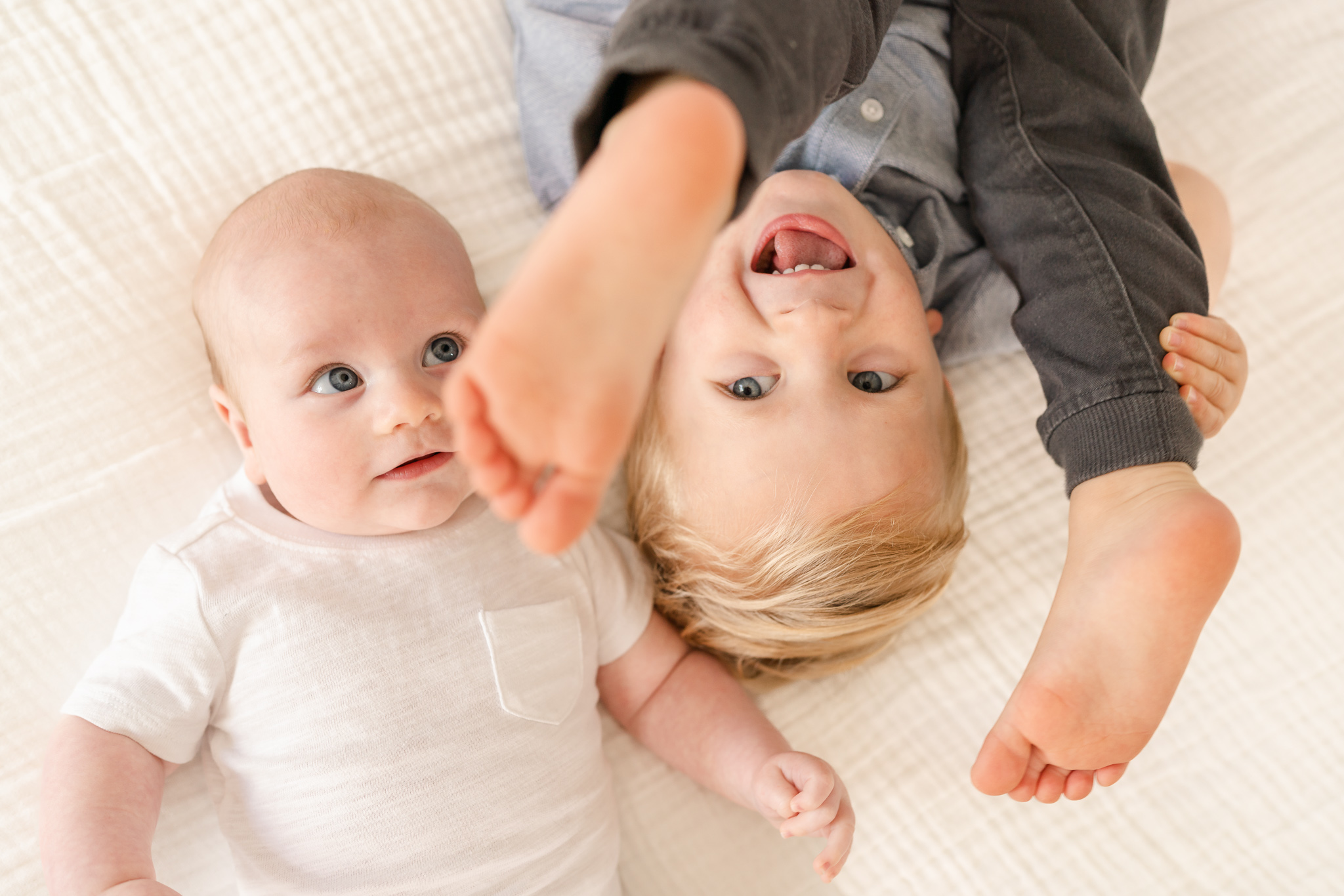 baby boy and big brother laying on a bed looking up at the camera