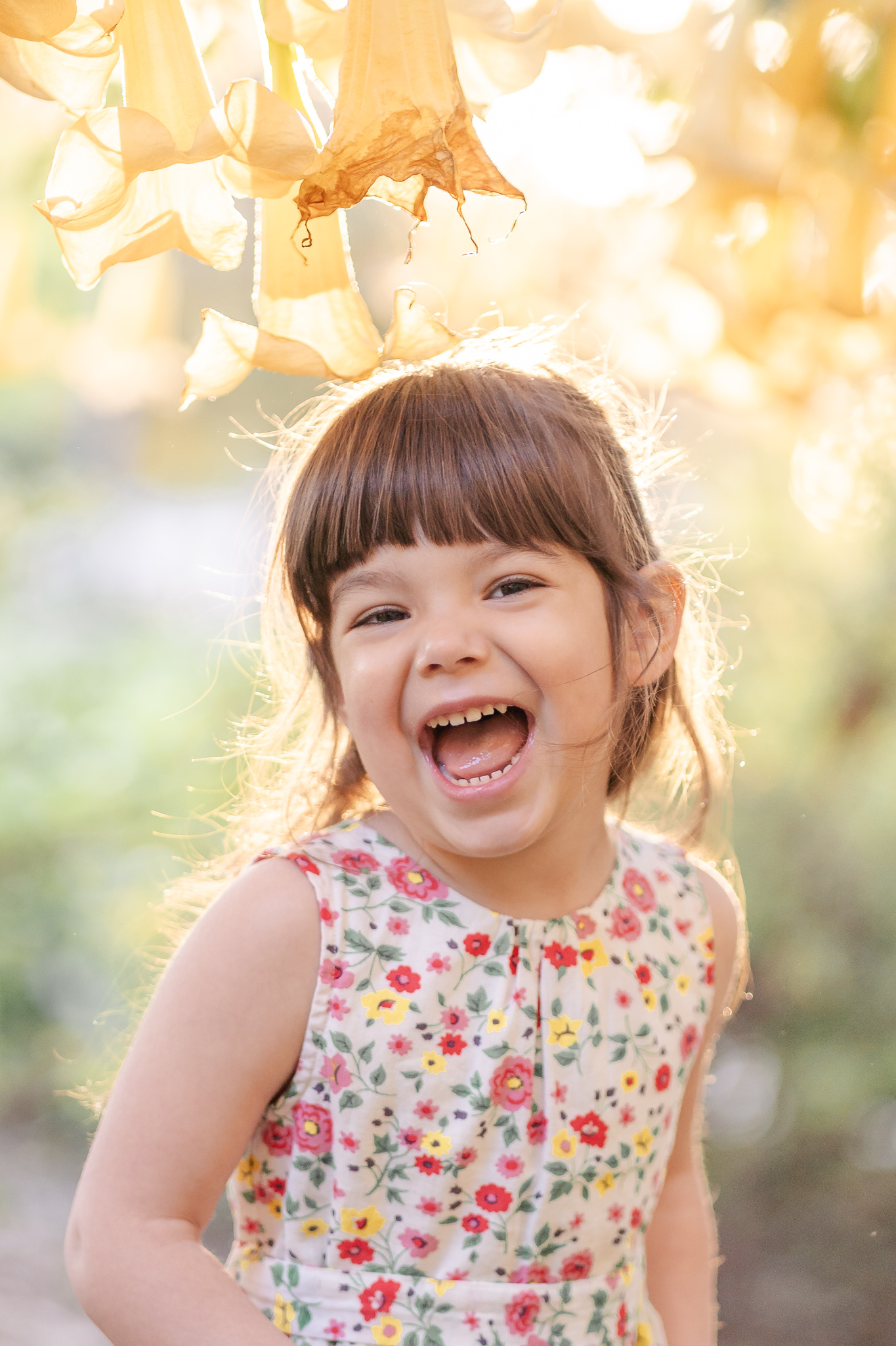 preschool girl smiling big at the camera standing under yellow flowers