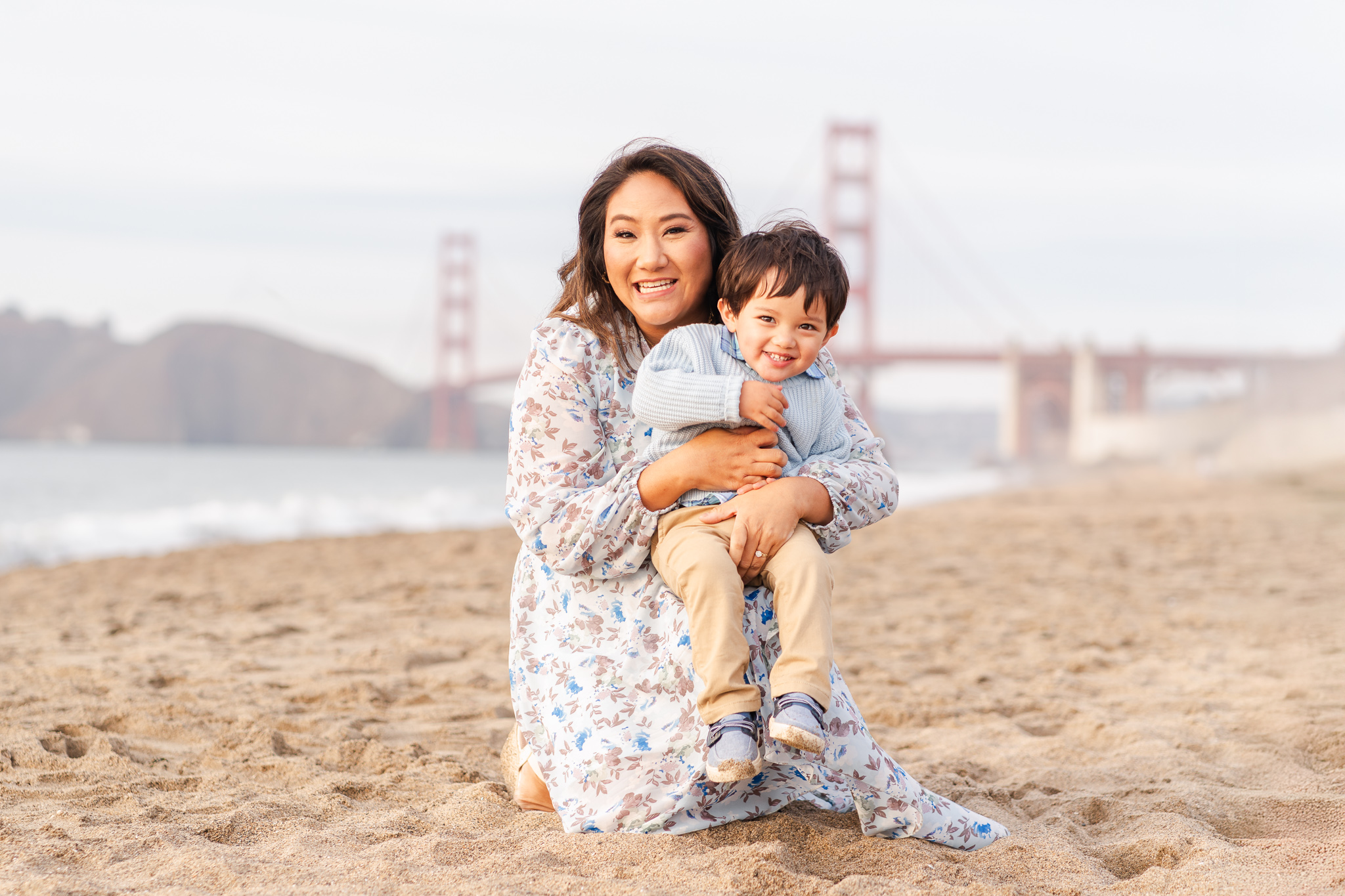 mom and son smiling and snuggling on baker beach in front of the golden gate bridge