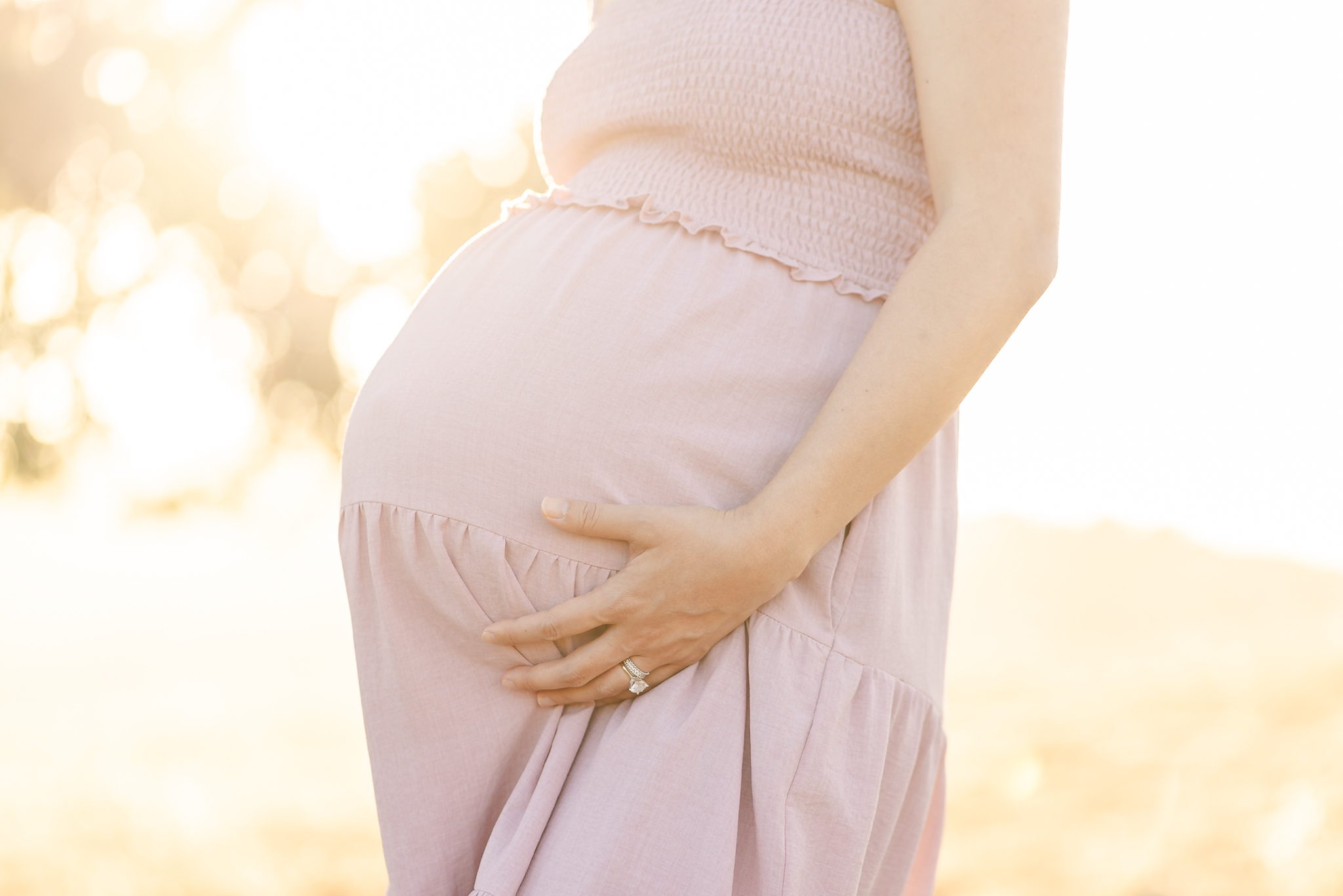 closeup of a pregnant woman wearing a pink dress and holding her belly