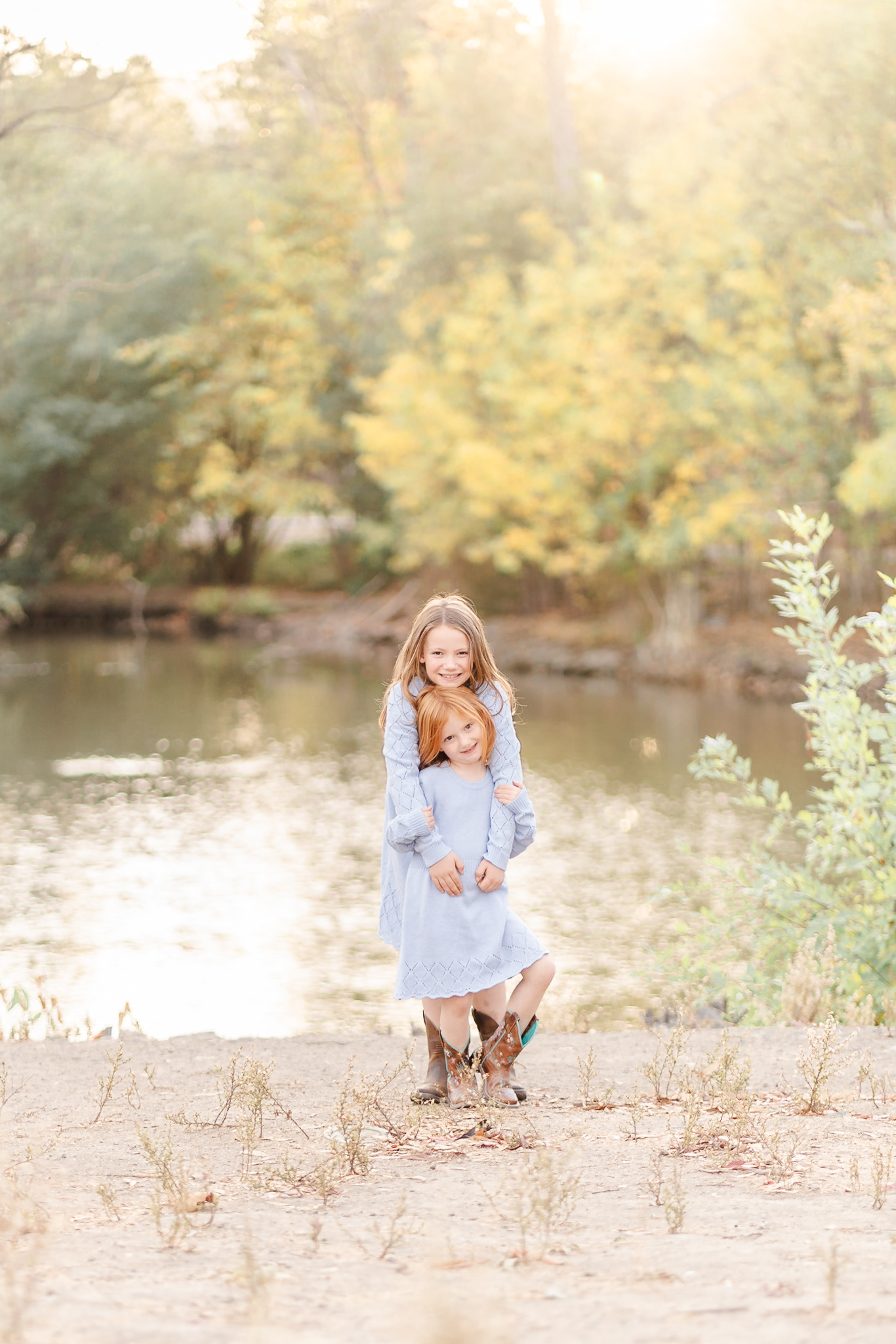 A couple of Los Gatos kids standing near the creek at Vasona Lake. They are girls wearing blue dresses and there is fall color behind them.